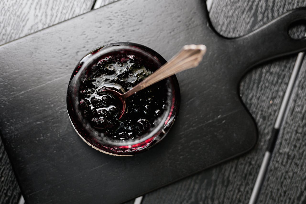 The Art of Drawing Readers In: Your attractive post title goes here Aerial shot of a jar of dark jam on a wooden board with a spoon, perfect for food photography.